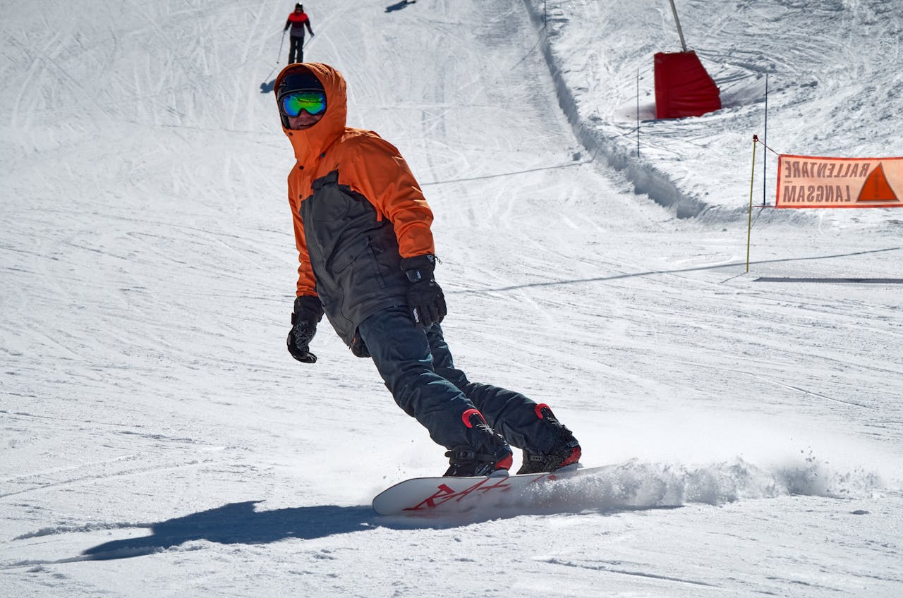 Strona Główna Snowboarder in orange jacket performing a carve on a snowy piste during winter.